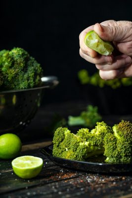 Someone splashing lime over cooked broccoli on a plate